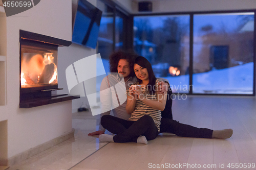 Image of happy multiethnic couple sitting in front of fireplace