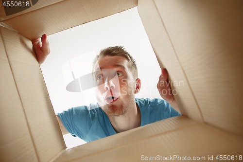 Image of Man smiling, unpacking and opening carton box and looking inside