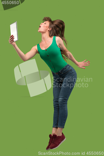 Image of Image of young woman over green background using laptop computer or tablet gadget while jumping.