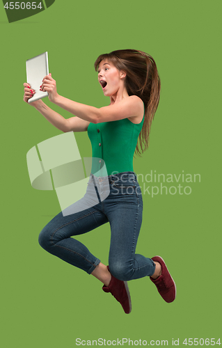 Image of Image of young woman over green background using laptop computer or tablet gadget while jumping.