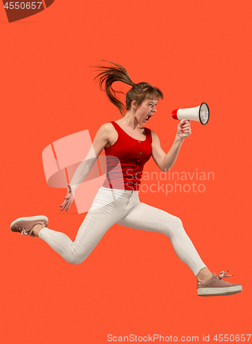 Image of Beautiful young woman jumping with megaphone isolated over red background