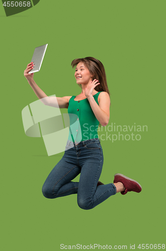 Image of Image of young woman over green background using laptop computer or tablet gadget while jumping.