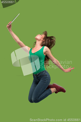 Image of Image of young woman over green background using laptop computer or tablet gadget while jumping.