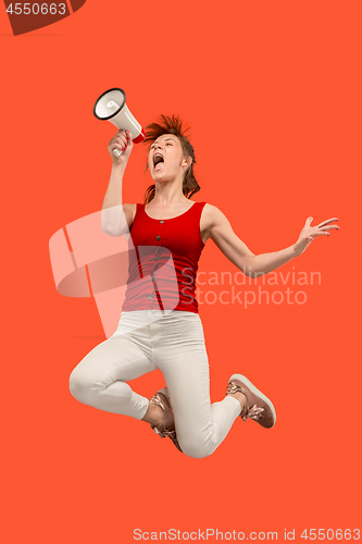 Image of Beautiful young woman jumping with megaphone isolated over red background