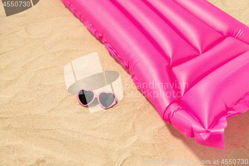 Image of sunglasses and pink swimming mattress on beach