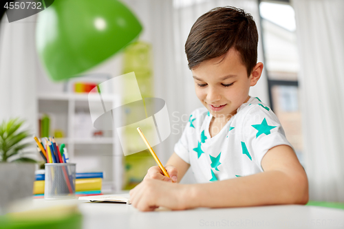 Image of happy boy writing or drawing to notebook at home