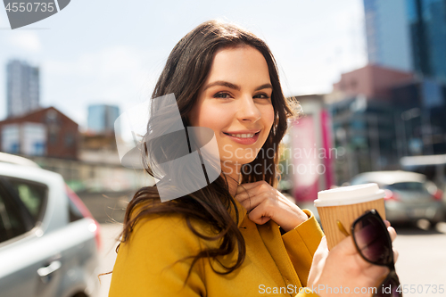 Image of happy young woman drinking coffee on city street