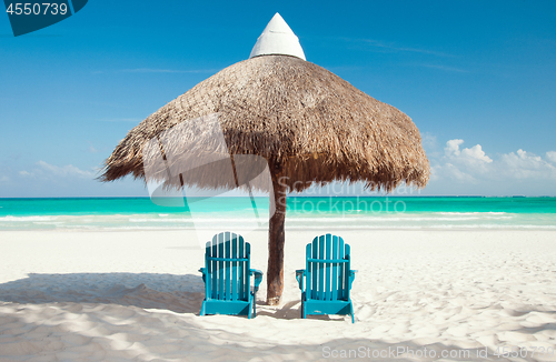 Image of two sun chairs under palapa on tropical beach