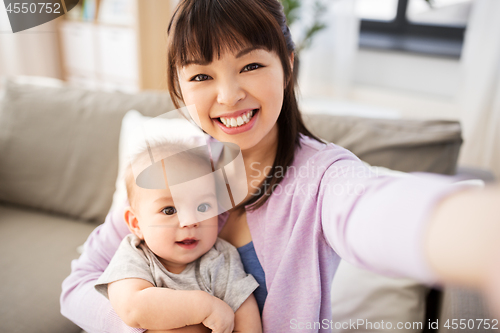 Image of asian mother with baby son taking selfie at home