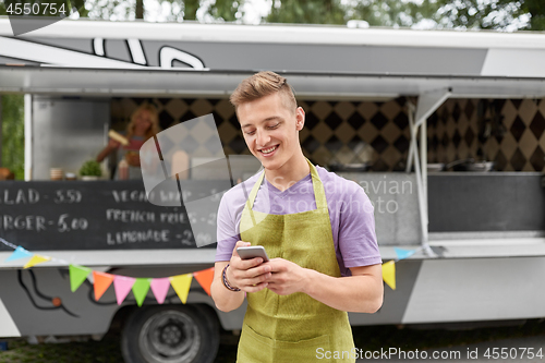 Image of salesman in apron with smartphone at food truck