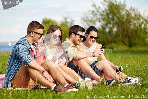 Image of smiling friends with smartphones sitting on grass