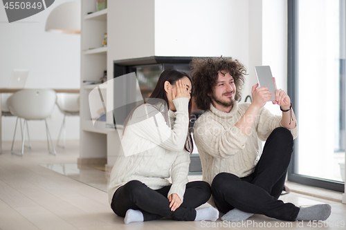 Image of multiethnic couple using tablet computer in front of fireplace