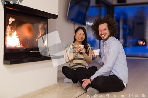 Image of happy multiethnic couple sitting in front of fireplace