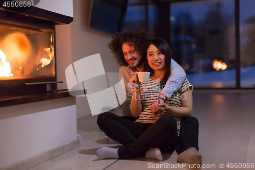 Image of happy multiethnic couple sitting in front of fireplace