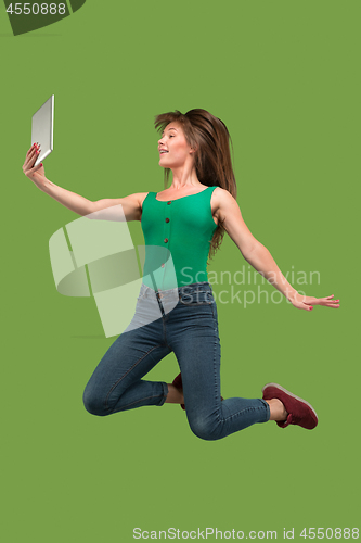 Image of Image of young woman over green background using laptop computer or tablet gadget while jumping.