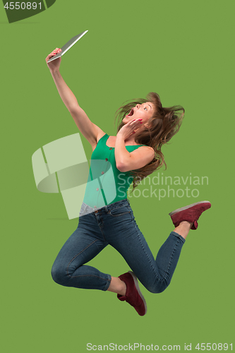 Image of Image of young woman over green background using laptop computer or tablet gadget while jumping.