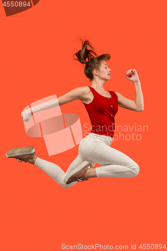 Image of Freedom in moving. Pretty young woman jumping against orange background