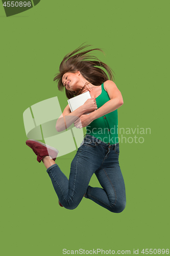 Image of Image of young woman over green background using laptop computer or tablet gadget while jumping.