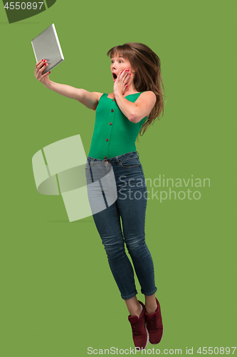 Image of Image of young woman over green background using laptop computer or tablet gadget while jumping.
