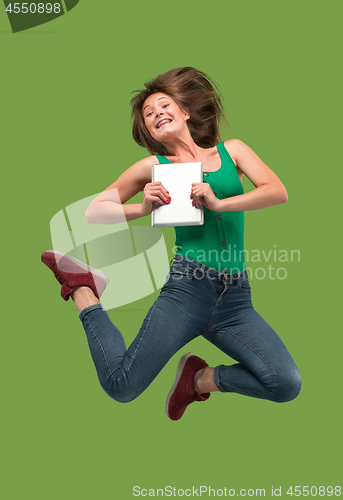 Image of Image of young woman over green background using laptop computer or tablet gadget while jumping.