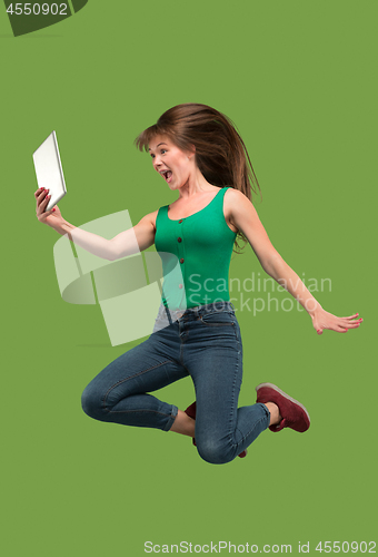 Image of Image of young woman over green background using laptop computer or tablet gadget while jumping.