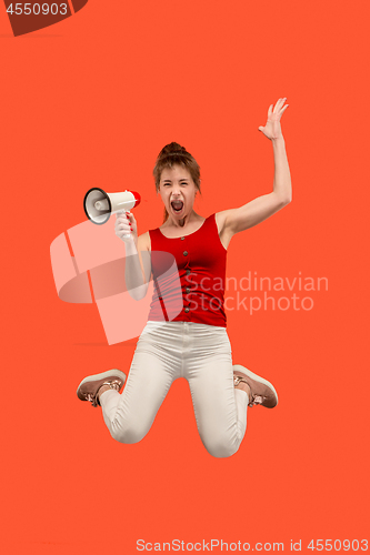 Image of Beautiful young woman jumping with megaphone isolated over red background