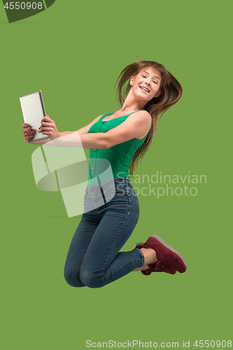 Image of Image of young woman over green background using laptop computer or tablet gadget while jumping.