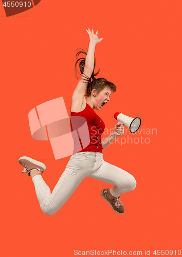 Image of Beautiful young woman jumping with megaphone isolated over red background