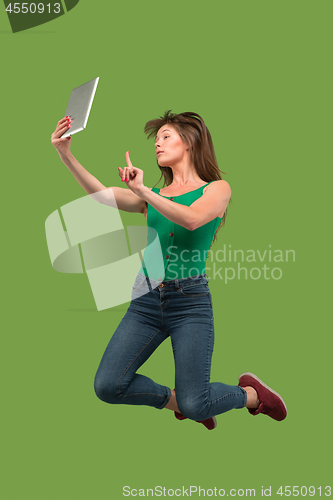 Image of Image of young woman over green background using laptop computer or tablet gadget while jumping.