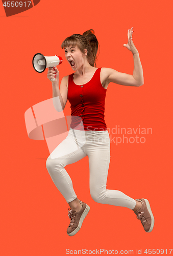 Image of Beautiful young woman jumping with megaphone isolated over red background