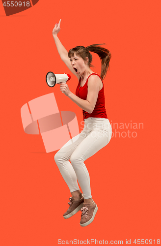 Image of Beautiful young woman jumping with megaphone isolated over red background