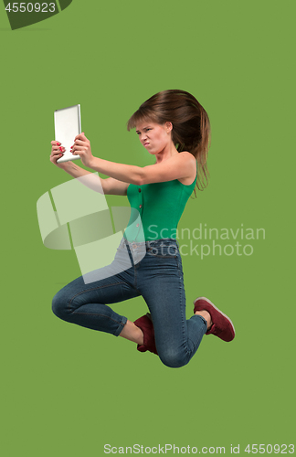 Image of Image of young woman over green background using laptop computer or tablet gadget while jumping.