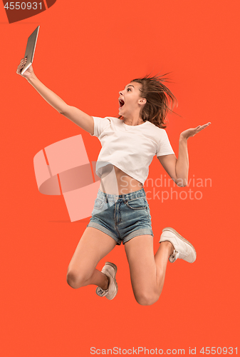 Image of Image of young woman over red background using laptop computer or tablet gadget while jumping.