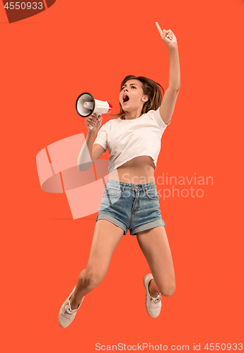 Image of Beautiful young woman jumping with megaphone isolated over red background