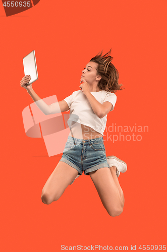 Image of Image of young woman over red background using laptop computer or tablet gadget while jumping.