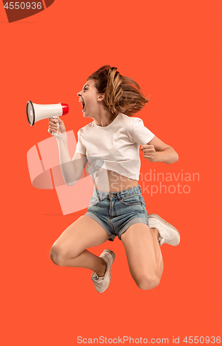 Image of Beautiful young woman jumping with megaphone isolated over red background