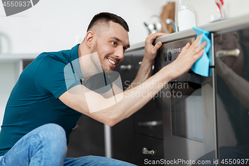 Image of man with rag cleaning oven door at home kitchen