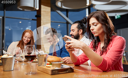 Image of bored woman messaging on smartphone at restaurant