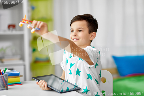 Image of boy with tablet computer and toy airplane at home