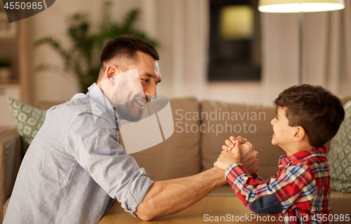 Image of happy father and little son arm wrestling at home