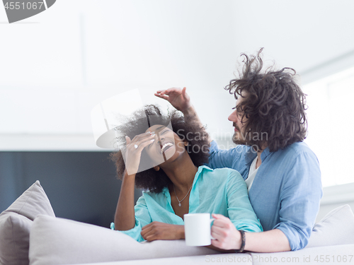 Image of multiethnic couple sitting on sofa at home drinking coffe