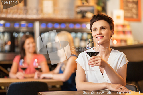 Image of happy woman drinking red wine at bar or restaurant