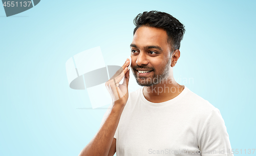 Image of smiling indian man cleaning face with cotton pad