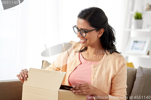 Image of happy indian woman opening parcel box at home