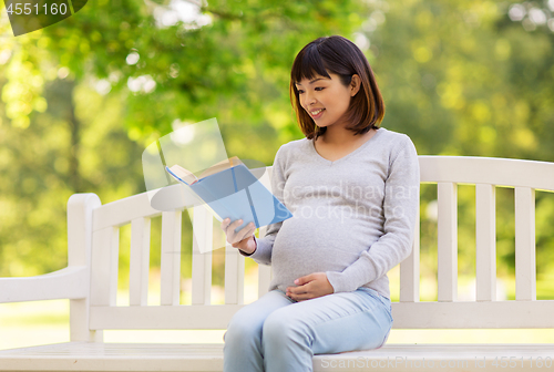 Image of happy pregnant asian woman reading book at park