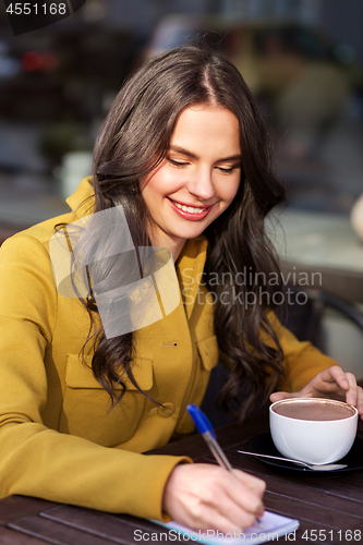 Image of happy woman with notebook drinking cocoa at cafe