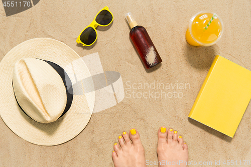 Image of feet, hat, shades, sunscreen and juice on beach
