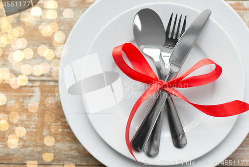 Image of cutlery tied with red ribbon on set of plates