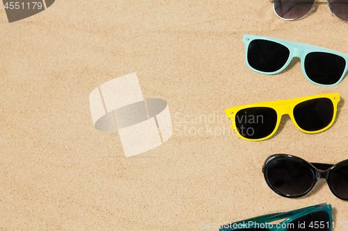 Image of different sunglasses on beach sand