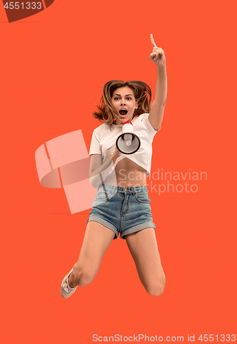 Image of Beautiful young woman jumping with megaphone isolated over red background